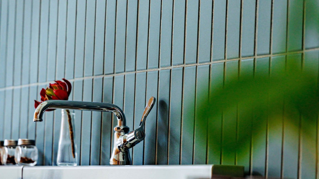 A chrome kitchen faucet against a vertical blue tiled backsplash.