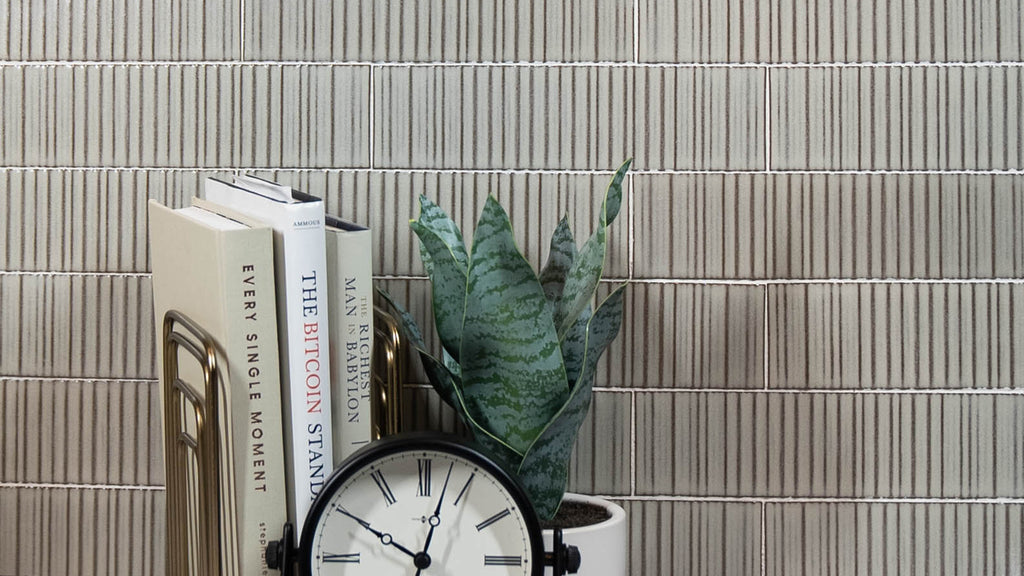 Textured beige fluted subway tile backsplash styled with a snake plant, books, and a classic desk clock.