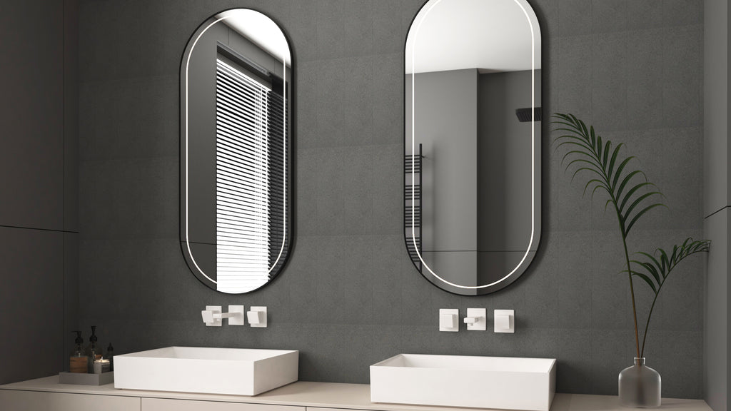 Modern bathroom vanity with double white vessel sinks, dark gray wall tile, and two backlit oval mirrors.