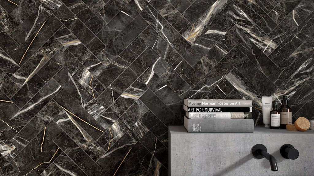 A stack of books and toiletries on a concrete ledge next to a black faucet against a black marbled herringbone-tiled wall.