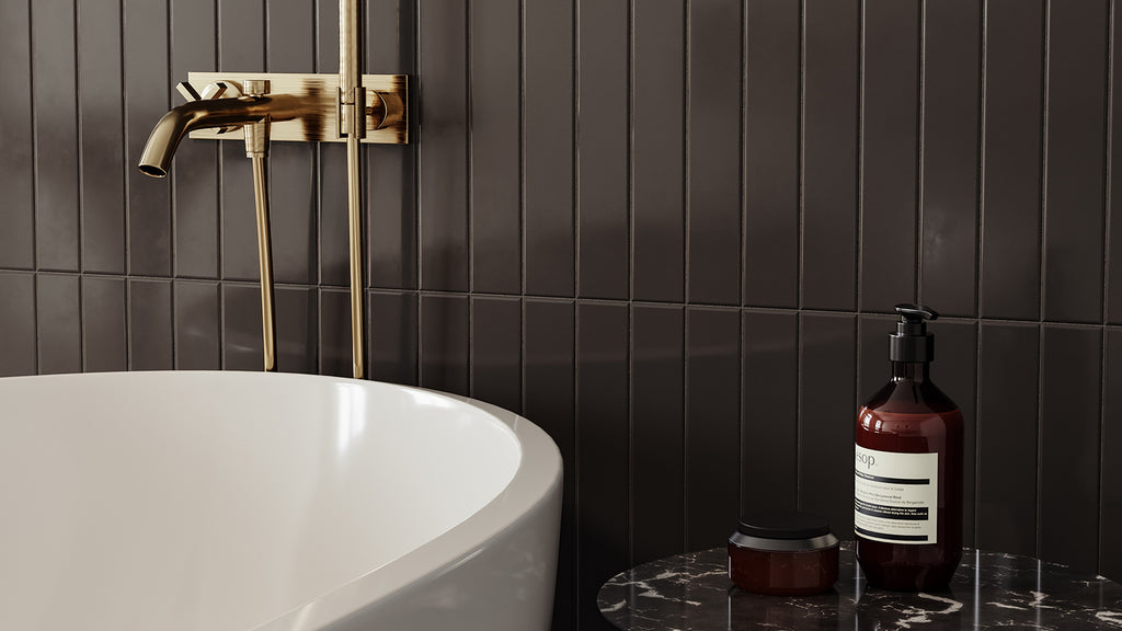 Luxury bathroom detail with a dark grey vertically stacked finger tile accent wall, gold fixtures, and a freestanding tub.