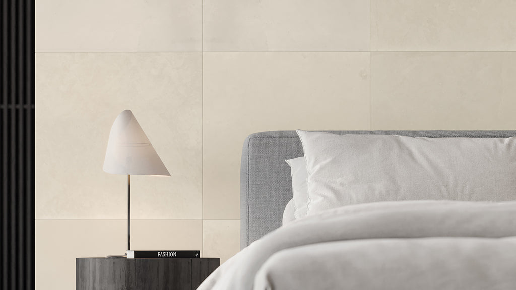 Minimalist bedroom interior featuring large off-white stone-look wall tiles, a grey headboard, and a stylish bedside lamp.
