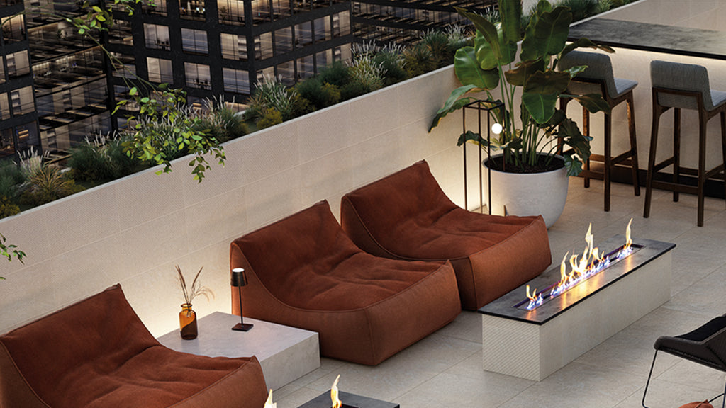 A high-angle view of a modern rooftop terrace featuring brown lounge chairs, a linear fire pit, and bar seating overlooking city buildings.