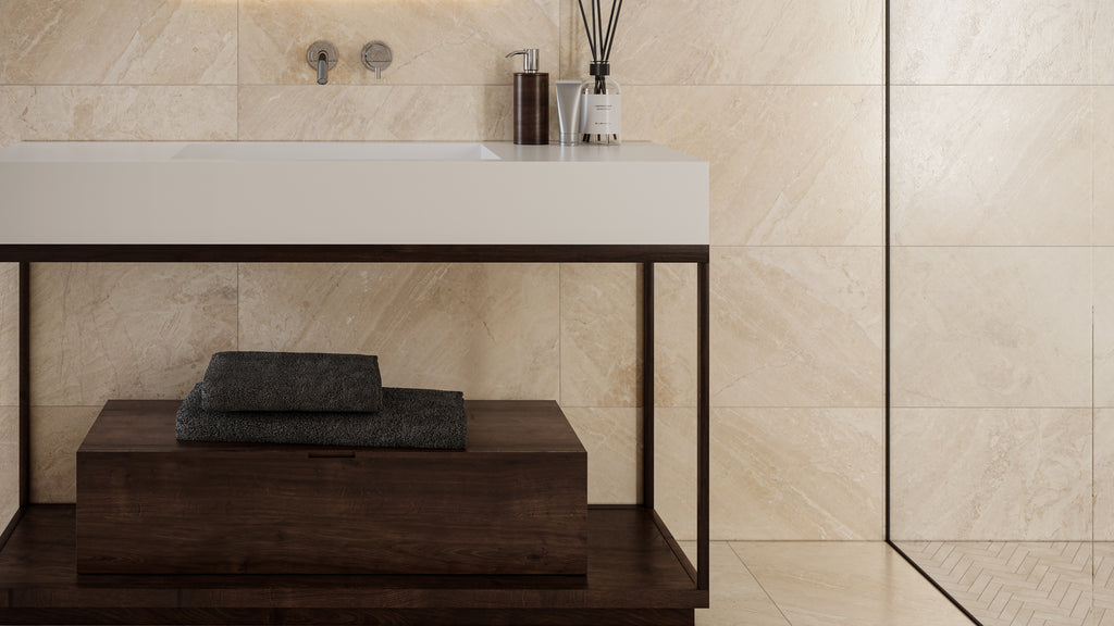 Close-up of a luxury bathroom featuring warm beige marble-look wall tiles, a white basin, and a dark wood vanity stand.