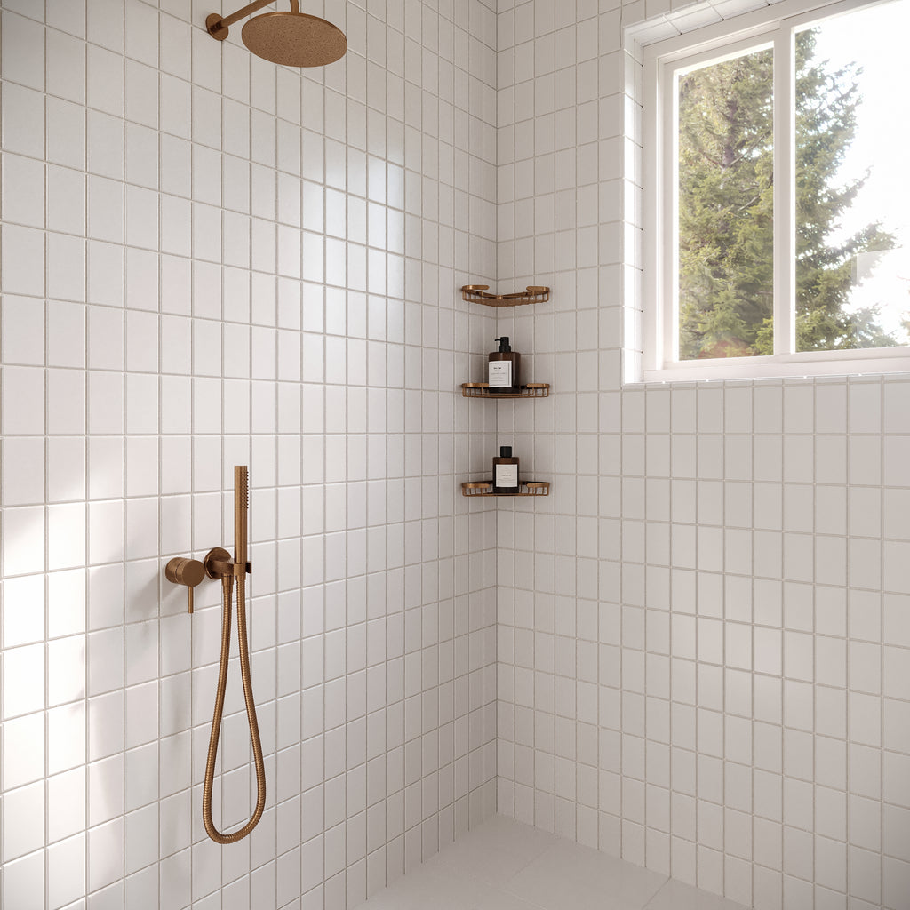 Minimalist shower featuring a white stack bond square tile wall, brushed bronze fixtures, and three tiered corner shelves near a window.