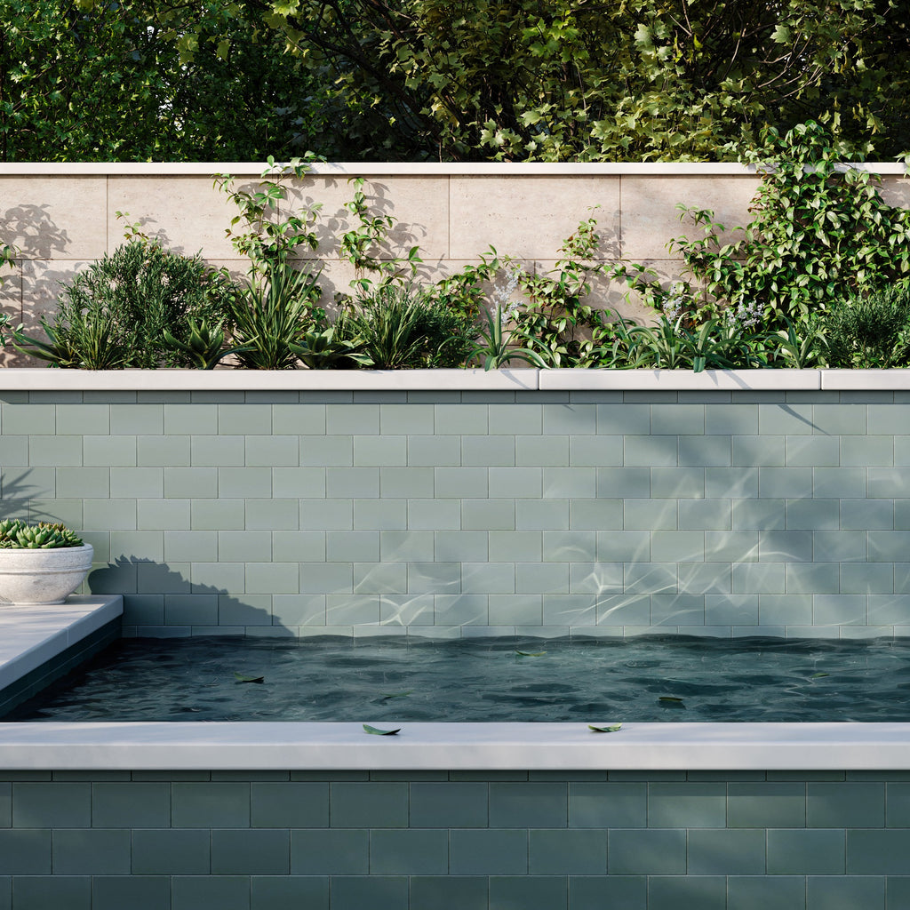 Luxury swimming pool design with light green subway tile walls, stone capping, and a raised planter bed filled with lush greenery.