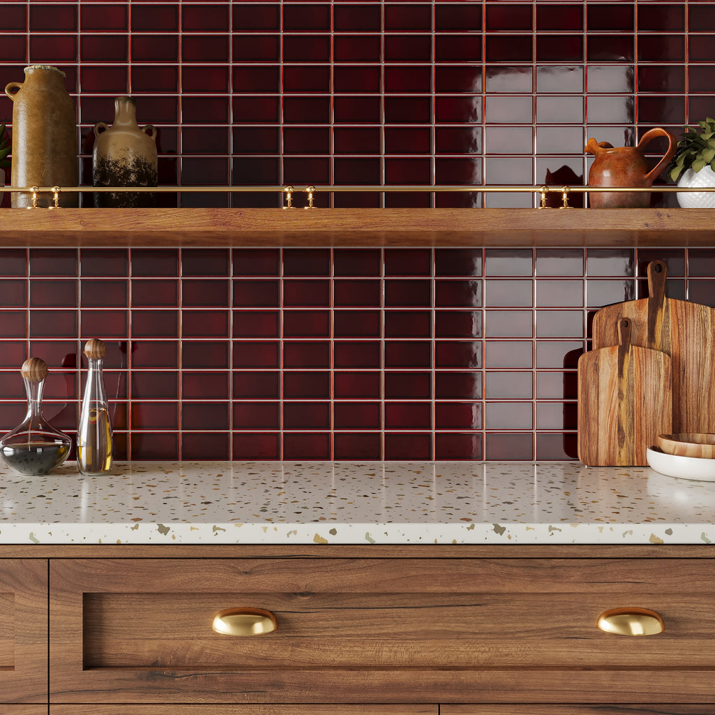Rustic kitchen featuring a glossy deep red square tile backsplash, warm wood cabinetry with brass cup pulls, and terrazzo countertops.