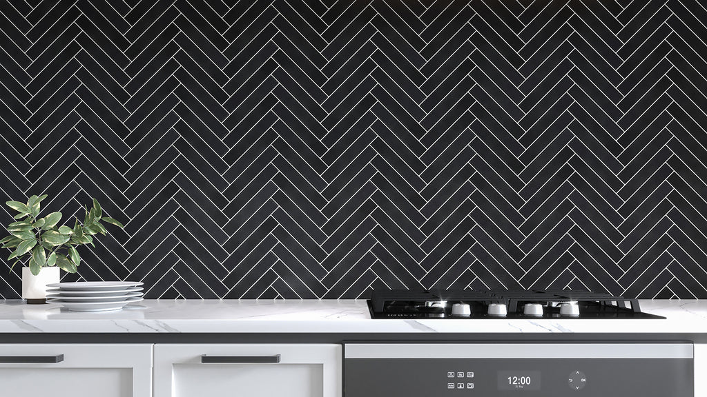 A close-up view of a black herringbone tile backsplash behind a white marble countertop with a gas stovetop.