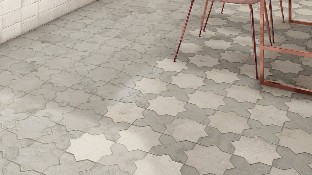 A ground-level view of light gray interlocking star-and-cross floor tiles with a partial view of a copper-legged chair.