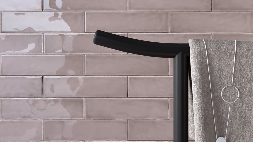 A close-up view of a matte black towel rack holding a textured beige towel against a glossy, light mauve subway-tiled wall.